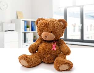 medicine, healthcare and oncology concept - teddy bear toy with pink breast cancer awareness ribbon over medical office at hospital background