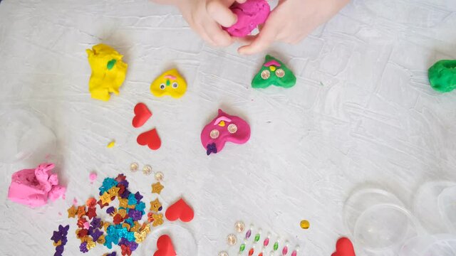 Child playing with colorful modeling plasticine  with  beads and sequins and sculpting heart figure. Home Education game with clay. Early development concept