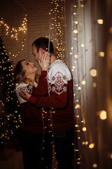 A guy and a girl in identical sweaters celebrate Christmas. A loving couple enjoy each other at the Christmas tree. New Year's love story.