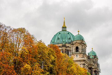 Fototapeta na wymiar The dome of the Berlin Cathedral ( Berliner Dom ) and the colorful autumn crowns of the trees in the foreground on a cloudy day. Autumn in Berlin, Germany.