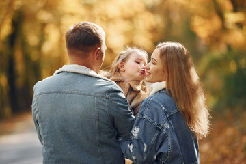 Fototapeta premium Little girl with her parents. Happy family is in the park at autumn time together