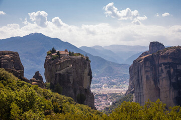 Fototapeta na wymiar Beautiful scenic view of Orthodox Monastery of Áyios Ayía Triáda (Holy Trinity) on cliff, immense monolithic pillar, at the background of stone wall and rock formations of Meteora mountain, Greece.