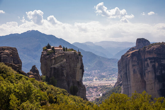 Beautiful scenic view of Orthodox Monastery of Áyios Ayía Triáda (Holy Trinity) on cliff, immense monolithic pillar, at the background of stone wall and rock formations of Meteora mountain, Greece.