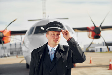 Pilot in formal black uniform is standing outdoors near plane