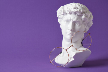 Stylish eye glasses with gypsum sculpture on a purple trendy color background, copy space David bust