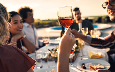 Close up of woman hand holding a glass of red wine at dinner party with her friends.
