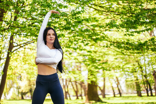 Girl stretches, prepares her body and muscles for a productive fitness workout. Flexible female sporty model in the city park. Image with copy space.