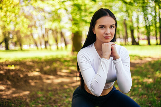 Girl stretches, prepares her body and muscles for a productive fitness workout, doing squats exercise. Flexible female sporty model in the city park. Image with copy space.

