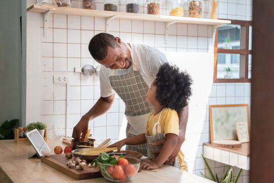 Loving Smiling African American Father and little boy cooking in kitchen at home, Happy Black Family