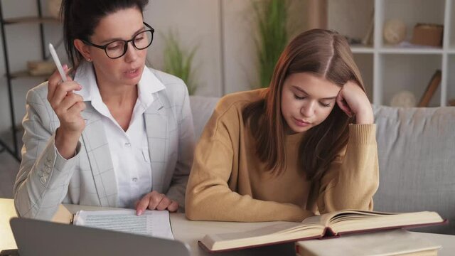 Exhausted Education. Bored Student. Home Training. Teaching Woman Talking To Falling Asleep Teenager Girl About Class Theme In Paper Notes Sitting Light Room Interior.