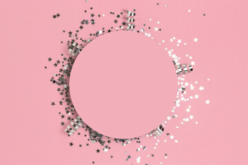 Round frame made of silver colored confetti on a pink pastel background.