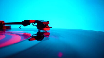 Black vinyl record spinning and play music on old turntable in rays of bright red and blue neon lights. Turntable needle on vinyl record, reads recording from grooves on disc. Close up. Slow motion.