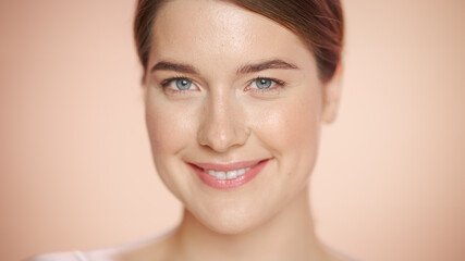 Close Up Female Beauty Portrait. Happy Caucasian Woman with Natural Healthy Skin, Brown Hair and Light Green Eyes Posing and Smiling. Wellness and Skincare Concept on Soft Isolated Background.