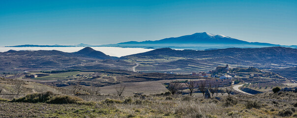 Panoramic view of fields, villages and snowy mountains, fogs in the valley, blue sky, spain.