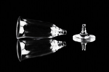 Broken wineglass lying on black reflecting surface, fractured stem of glass