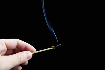 Almost extinct match with plume of smoke in fingers on black background