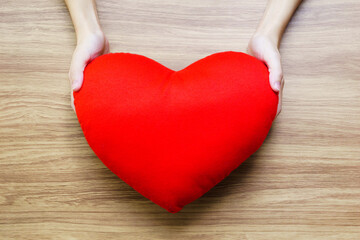 asian hand holding red heart pillow on wooden background