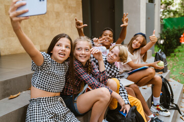 Multiracial pupils taking selfie photo on mobile phone by school