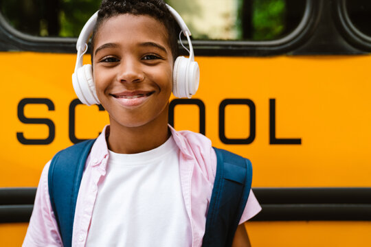Black boy in headphones smiling while standing by school bus
