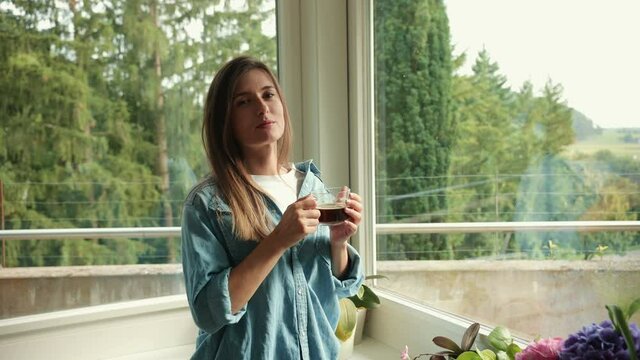 Beautiful caucasian woman drinking tea or coffee and looking to the camera at home. Health care, authenticity, sense of balance and calmness.