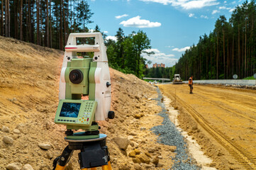 Surveyors equipment (theodolite or total positioning station) on the construction site of the road or building with construction machinery background