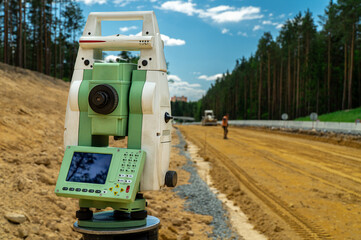 Surveyors equipment (theodolite or total positioning station) on the construction site of the road or building with construction machinery background