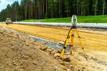 Surveyors equipment (theodolite or total positioning station) on the construction site of the road or building with construction machinery background