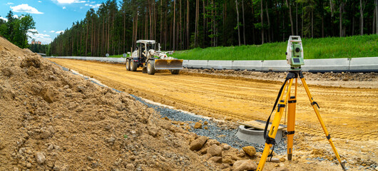 Surveyors equipment (theodolite or total positioning station) on the construction site of the road or building with construction machinery background