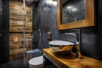Stylish dark bathroom interior with shower. Tiles imitating wood on the floor and on the wall