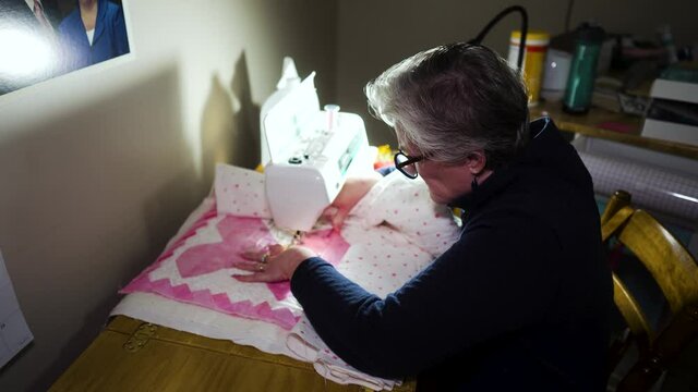 Senior woman using a sewing machine to stitch heart patterns on a handmade quilt