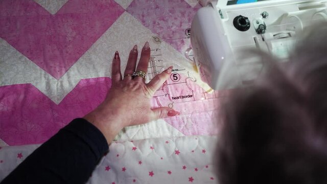 Woman using a sewing machine and a plastic template to sew a pattern on a quilt - over shoulder view