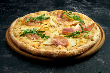 Pizza with jamon, pear and arugula on a black stone background. 45 degree angle view. Close-up, selective focus