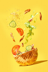 Pita with ingredients (meat, cheese, tomatoes, cucumbers) are flying into the shawarma on a yellow background. Close-up kebab sandwich