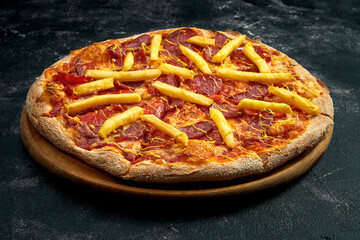 Pizza with salami, and smoked sausages, french fries on a black stone background. 45 degree angle view. Close-up, selective focus