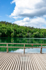 Fototapeta na wymiar green water lakes coast with wooden bridge, juicy green trees and deep sky