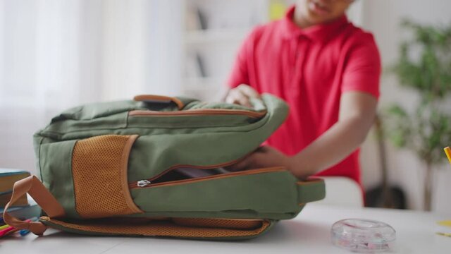 Black boy putting books in school bag, child development, education system