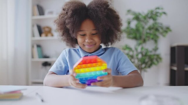 African American girl playing with pop it toy, pressing buttons, stress relief