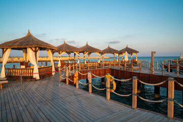 Wooden platform to enter the sea. Beach sun loungers under rustic straw umbrellas. a relaxing holiday.
