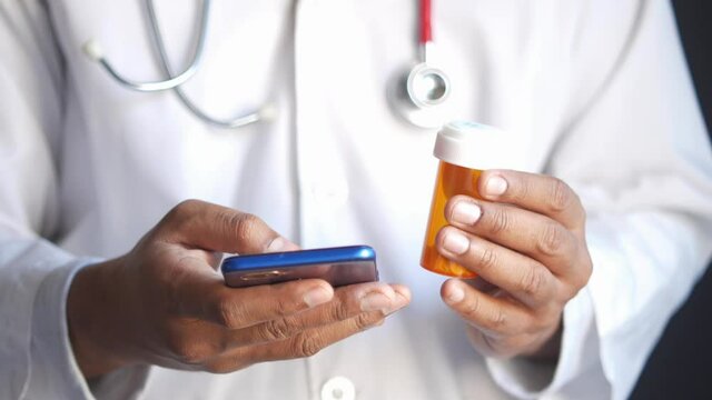 doctor in white coat using a smartphone and holding medical pill container 