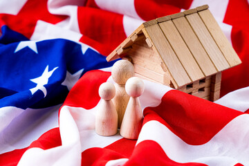 American family concept with wooden figurines of people and toy wooden house standing on the flag...