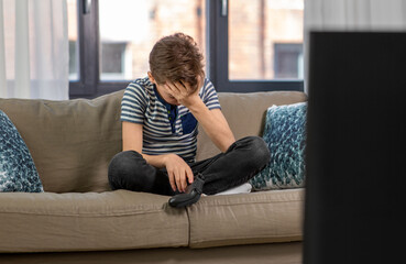 leisure, children, technology and people concept - upset boy with gamepad playing video game at home © Syda Productions