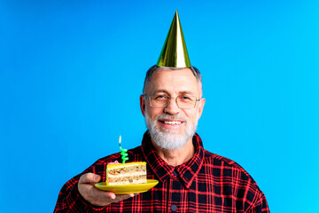 man wearing birthday hat with cake isolated on bright blue colour background, studio portrait