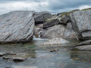 Water runs over the top of big grey stone boulders at water stream at arctic northern landscape in Swedish Lapland