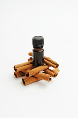 Small dark glass bottle on cinnamon sticks on white. Essential oil or extract. Cosmetic or food concept