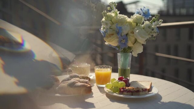 Perfect morning breakfast on balcony with tasty croissants, fresh juice, coffee and fruits. Sunny warm day. Sunlight in footage.