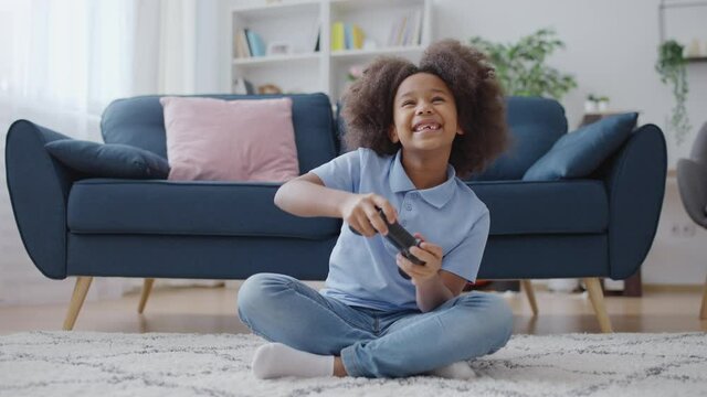 Smiling little girl playing video game at home, happy carefree childhood