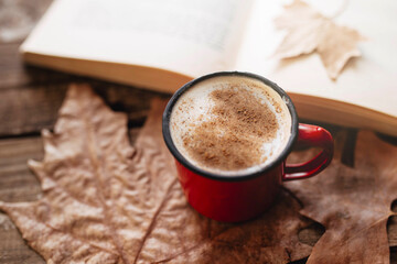 Morning routine. Coffee with mil cocoa and cinnamon. Reading a book in autumn. Wooden table with autumnal leaves.