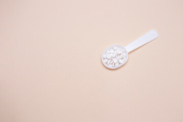 Concept of medicine, nursing and pharmacy. Teaspoon with pills on a beige background. Copy space.