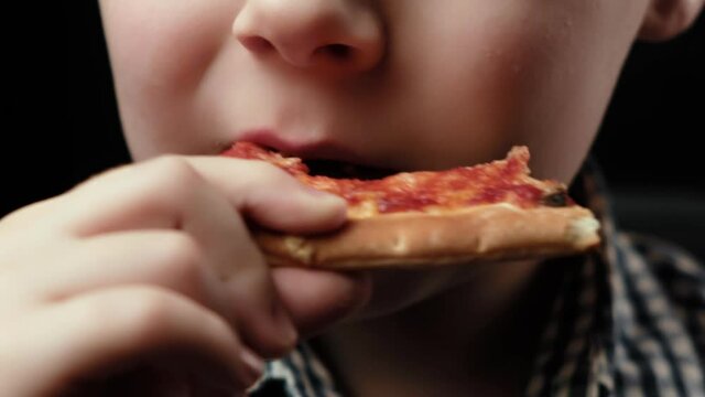 Young boy chews pizza. Close-up. Mouth and pizza. Dark background. Hunger, appetite.