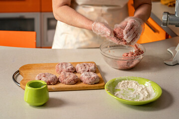 female hands in gloves form cutlets and roll them in flour 